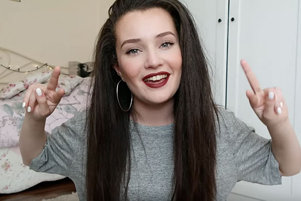 Video of a brunette with long hair smiles and shows with both hands peace