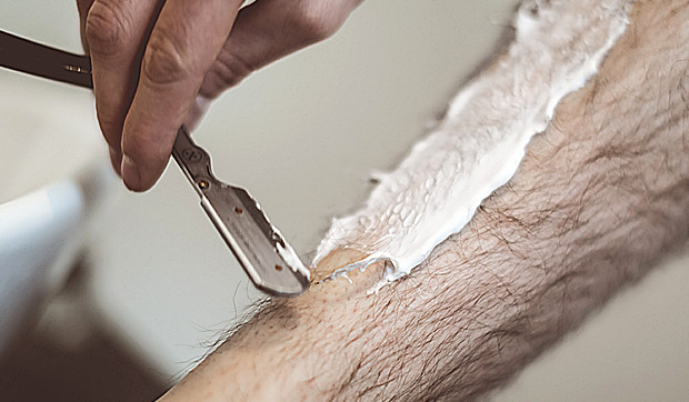 Man shaves his leg with a razor blade, shaving foam on a leg