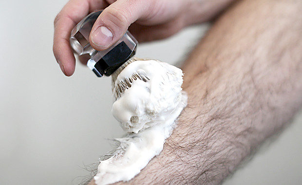 Man puts shaving foam with a shaving brush on his leg